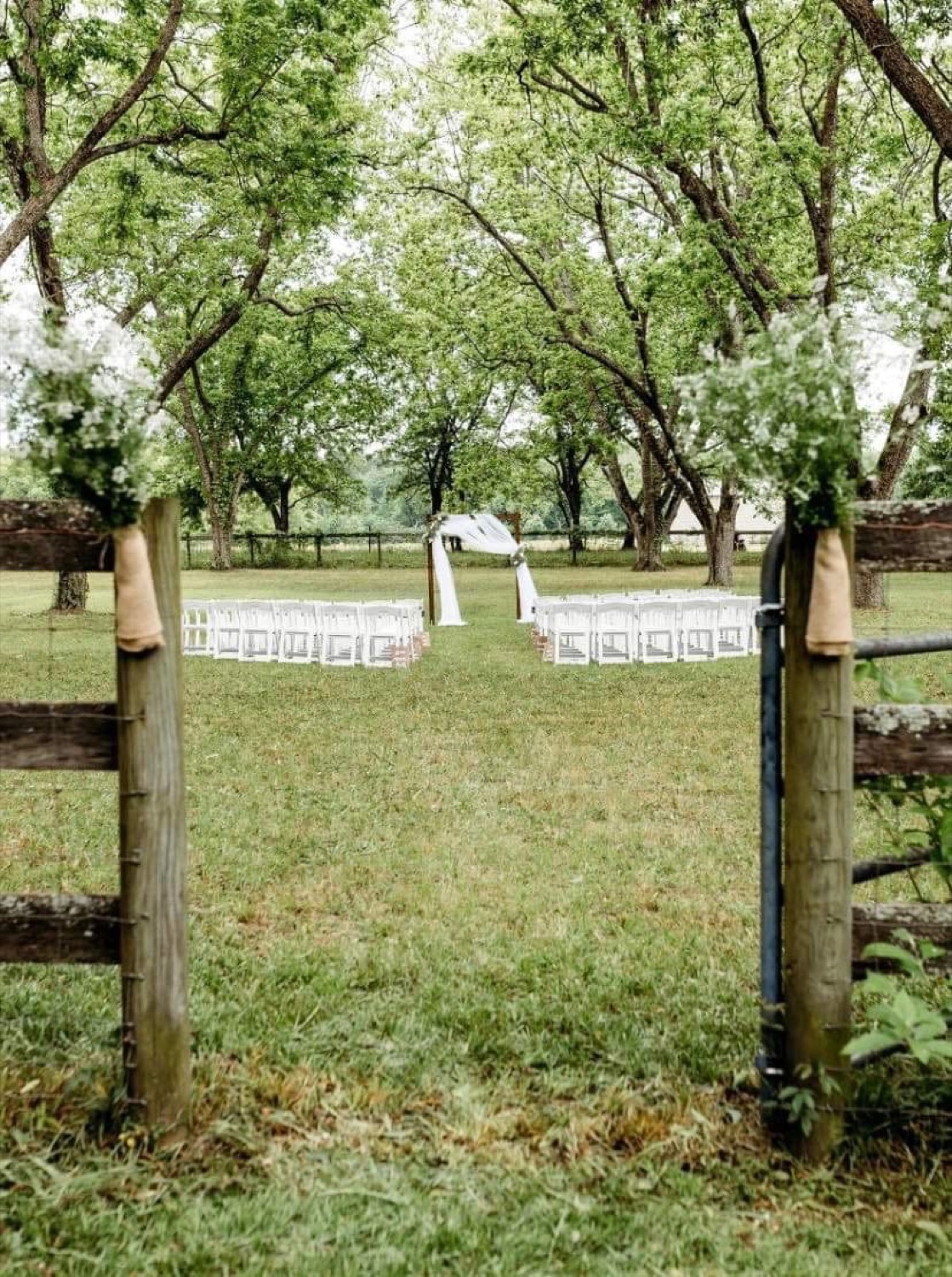 Outdoor wedding ceremony with white chairs and a draped arbor