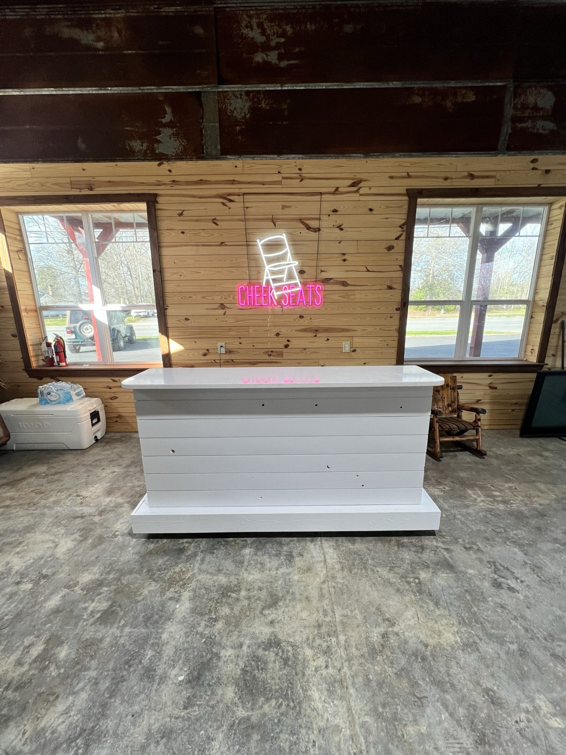 White mobile bar with the Cheek Seats neon sign